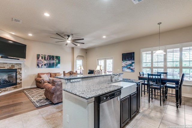 kitchen featuring visible vents, open floor plan, a kitchen island with sink, a stone fireplace, and dishwasher