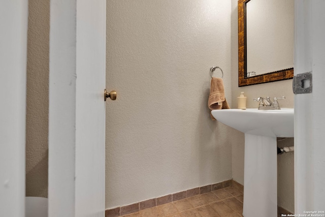 bathroom featuring a textured wall, tile patterned floors, and baseboards