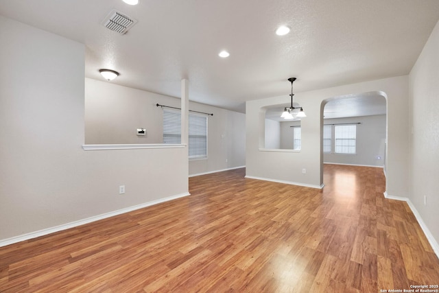 unfurnished room with arched walkways, visible vents, a textured ceiling, light wood-type flooring, and baseboards