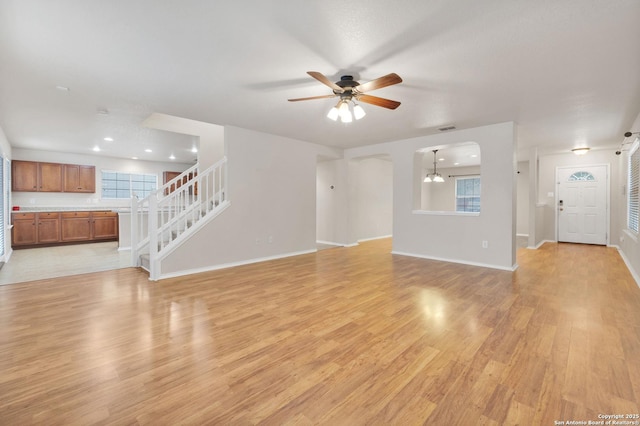 unfurnished living room featuring arched walkways, visible vents, baseboards, stairs, and light wood-type flooring