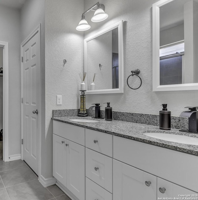 full bath featuring double vanity, tile patterned flooring, a sink, and a textured wall