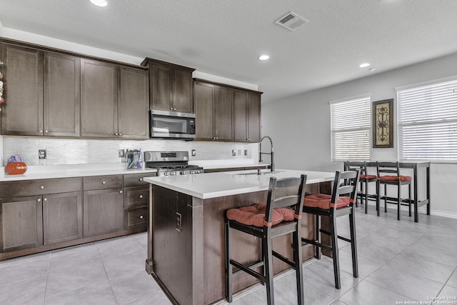 kitchen with stainless steel appliances, a sink, visible vents, tasteful backsplash, and a center island with sink