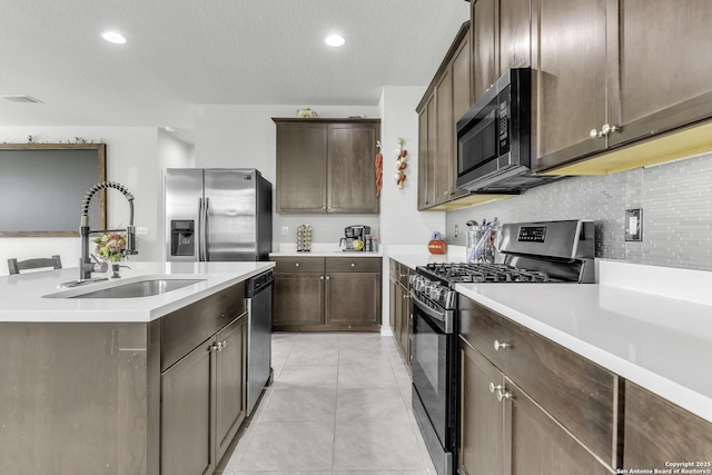 kitchen featuring stainless steel appliances, tasteful backsplash, light countertops, a sink, and dark brown cabinetry