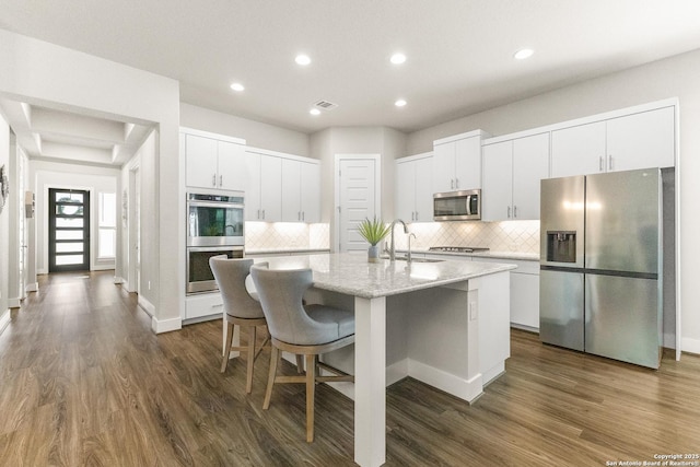 kitchen with a center island with sink, visible vents, dark wood-style floors, stainless steel appliances, and a sink