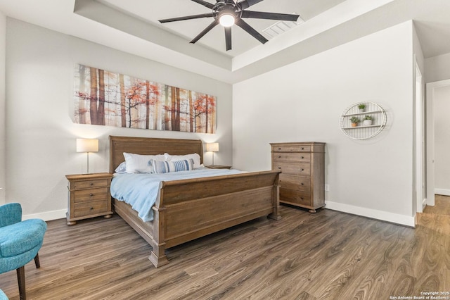 bedroom with a tray ceiling, wood finished floors, a ceiling fan, and baseboards