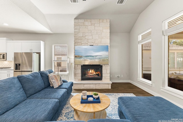 living room featuring visible vents, baseboards, dark wood-style flooring, vaulted ceiling, and a stone fireplace