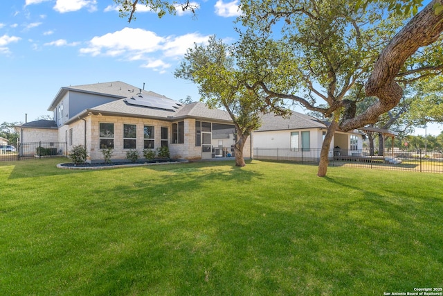 back of property featuring solar panels, a sunroom, a fenced backyard, stone siding, and a yard