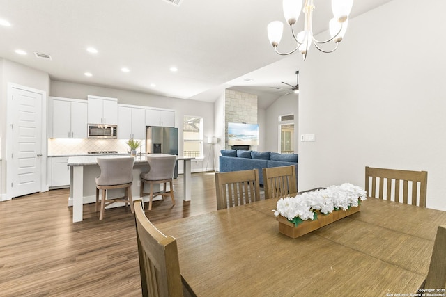 dining space with recessed lighting, visible vents, vaulted ceiling, wood finished floors, and ceiling fan with notable chandelier