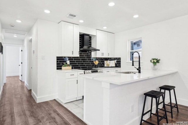 kitchen featuring wall chimney exhaust hood, visible vents, decorative backsplash, a sink, and a kitchen bar