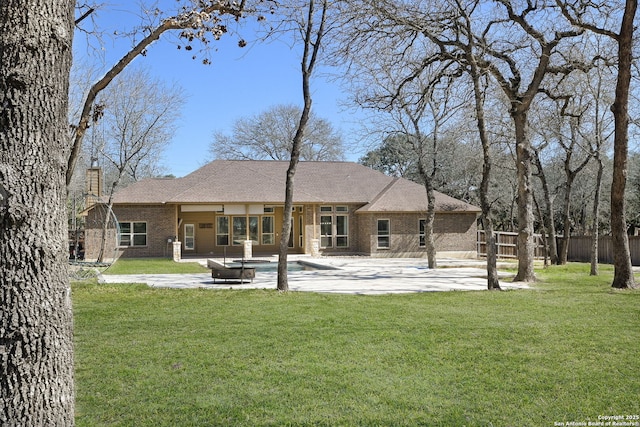 rear view of house featuring fence, a chimney, a lawn, a patio area, and brick siding