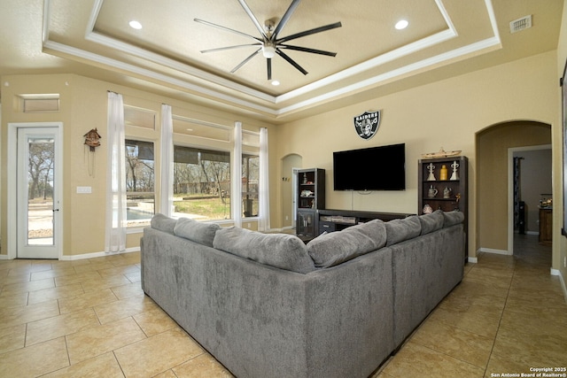 living area featuring a tray ceiling, visible vents, arched walkways, and baseboards