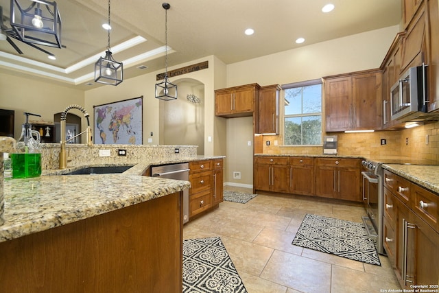 kitchen featuring decorative backsplash, appliances with stainless steel finishes, brown cabinetry, a raised ceiling, and a sink