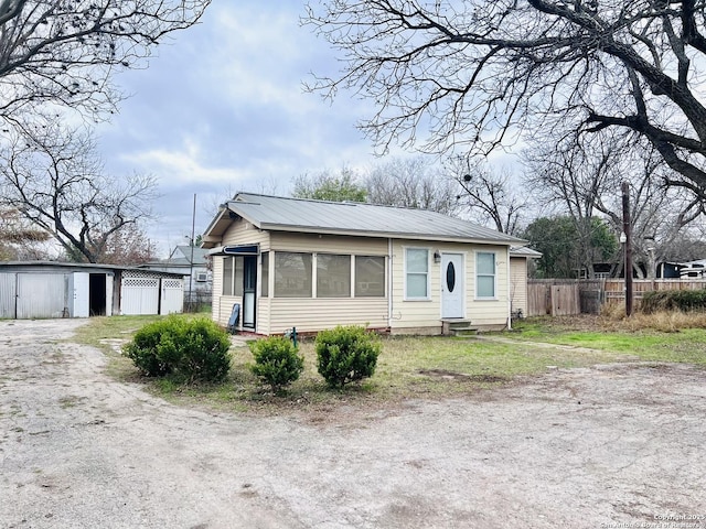 view of front facade featuring an outbuilding, entry steps, metal roof, fence, and driveway