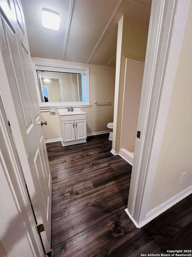 bathroom with toilet, wood finished floors, vanity, baseboards, and vaulted ceiling