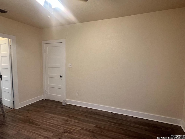 empty room with dark wood-type flooring, visible vents, and baseboards