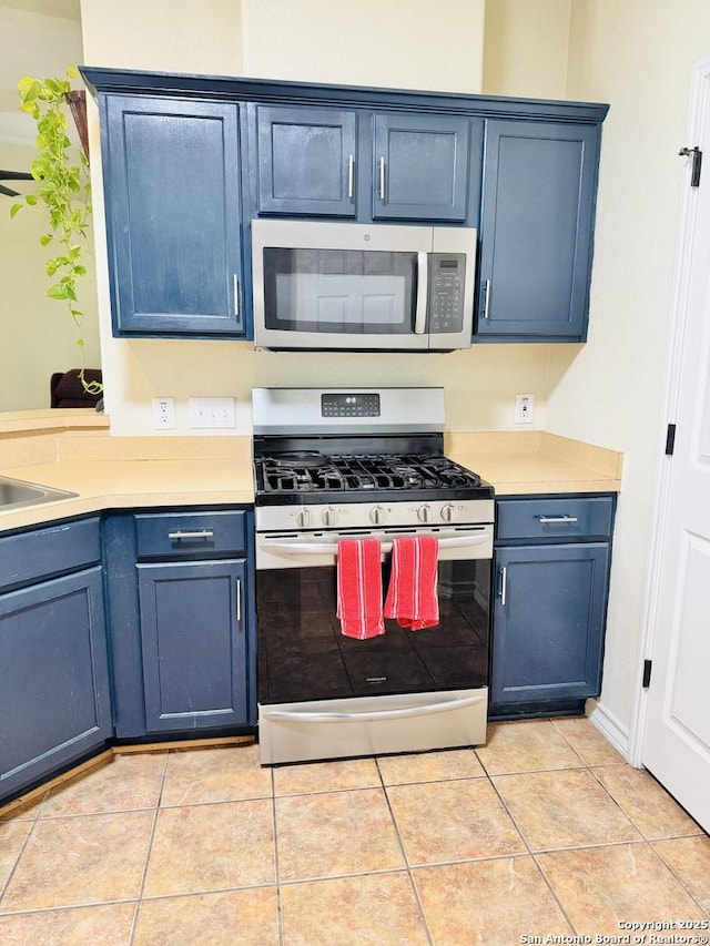 kitchen with light tile patterned floors, stainless steel appliances, blue cabinetry, and light countertops