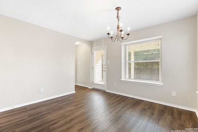 unfurnished room with dark wood-style floors, baseboards, arched walkways, and a chandelier