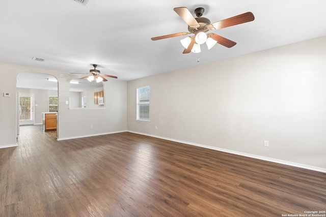 unfurnished living room with arched walkways, ceiling fan, dark wood-style flooring, visible vents, and baseboards