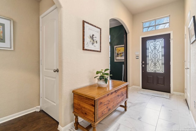 entryway featuring arched walkways, marble finish floor, and baseboards