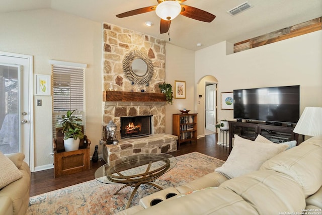 living room featuring arched walkways, lofted ceiling, visible vents, a stone fireplace, and wood finished floors