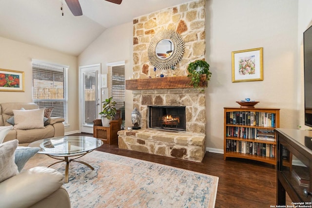 living area with lofted ceiling, a healthy amount of sunlight, dark wood finished floors, and a stone fireplace