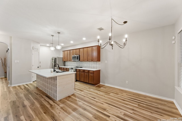 kitchen with a center island with sink, brown cabinetry, backsplash, stainless steel appliances, and a sink