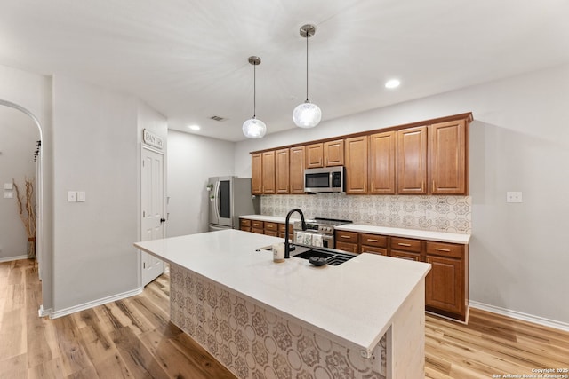 kitchen with appliances with stainless steel finishes, arched walkways, light wood-style flooring, and decorative backsplash