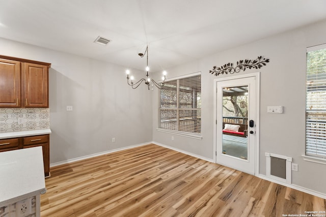 unfurnished dining area with visible vents, a notable chandelier, light wood-style flooring, and baseboards