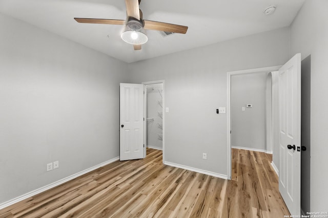 unfurnished bedroom with baseboards, ceiling fan, a walk in closet, light wood-style floors, and a closet