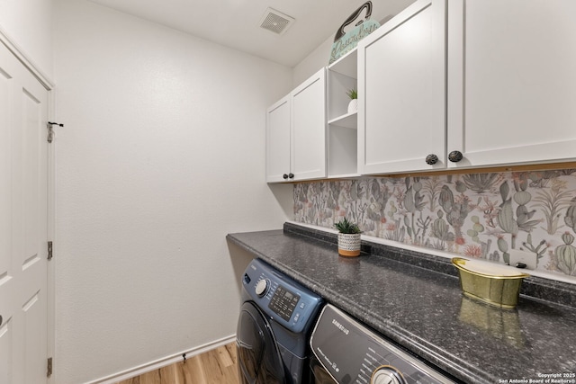 clothes washing area featuring light wood finished floors, visible vents, cabinet space, washing machine and dryer, and baseboards