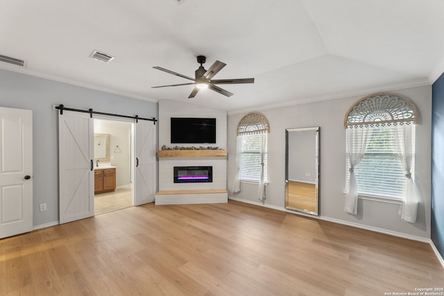 unfurnished living room with ceiling fan, a barn door, light wood-type flooring, and visible vents