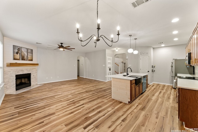 kitchen featuring arched walkways, a kitchen island with sink, a fireplace, a sink, and visible vents