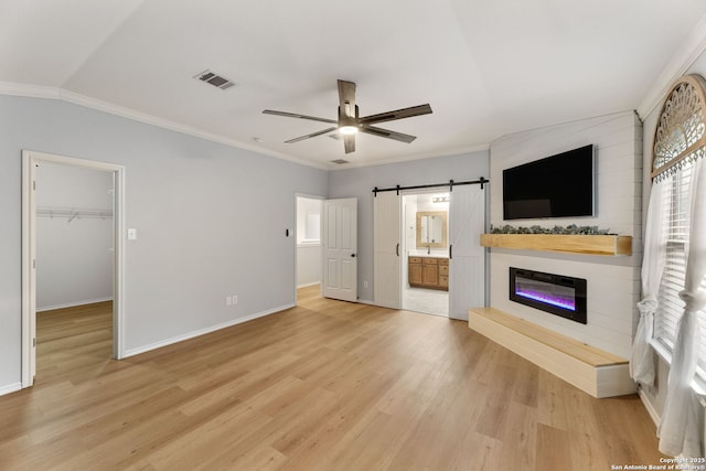 unfurnished living room with visible vents, a barn door, ornamental molding, a ceiling fan, and light wood-type flooring