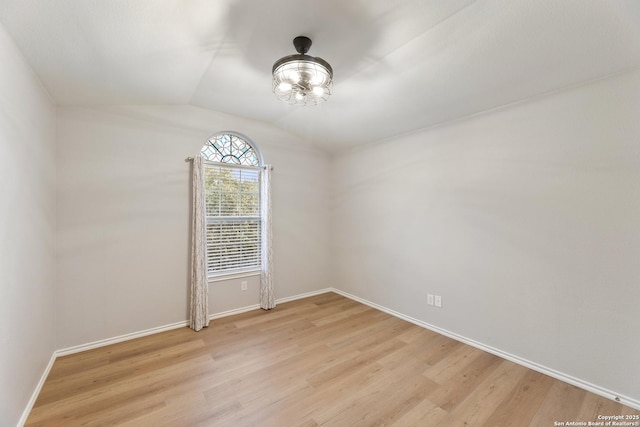 spare room featuring lofted ceiling, light wood-style flooring, and baseboards