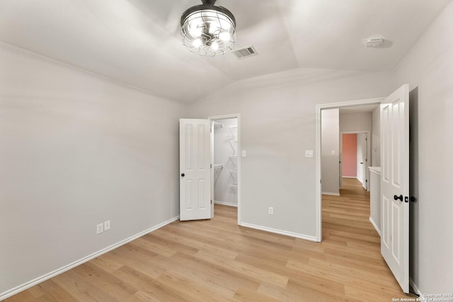 unfurnished bedroom featuring vaulted ceiling, light wood-type flooring, visible vents, and baseboards