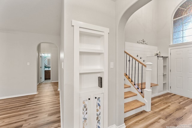 foyer entrance with arched walkways, wood finished floors, stairs, and baseboards