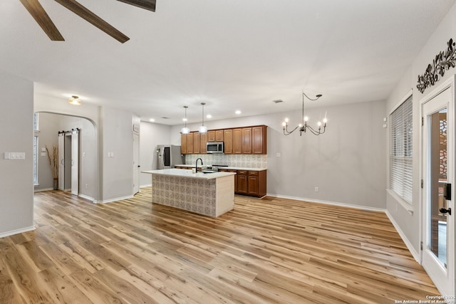 kitchen featuring light wood finished floors, arched walkways, a kitchen island with sink, stainless steel appliances, and light countertops