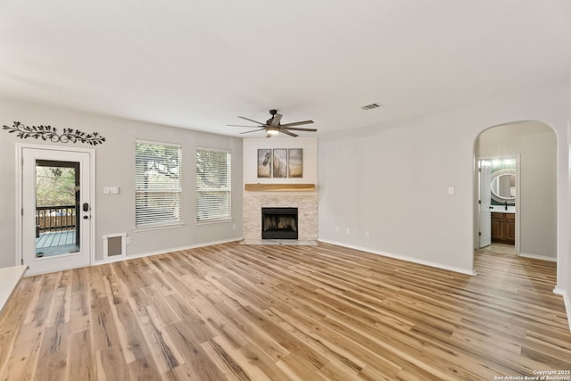 unfurnished living room featuring light wood-style flooring, a fireplace, visible vents, and arched walkways