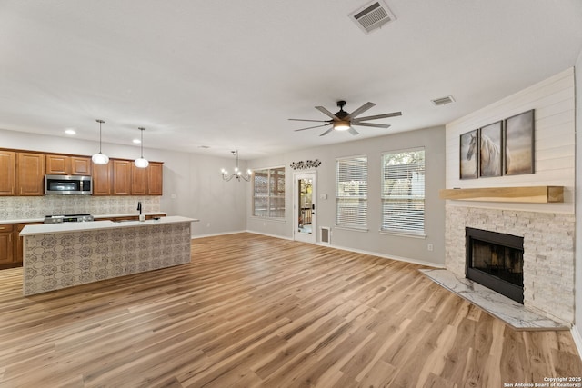 living area with a fireplace, visible vents, light wood-style flooring, baseboards, and ceiling fan with notable chandelier