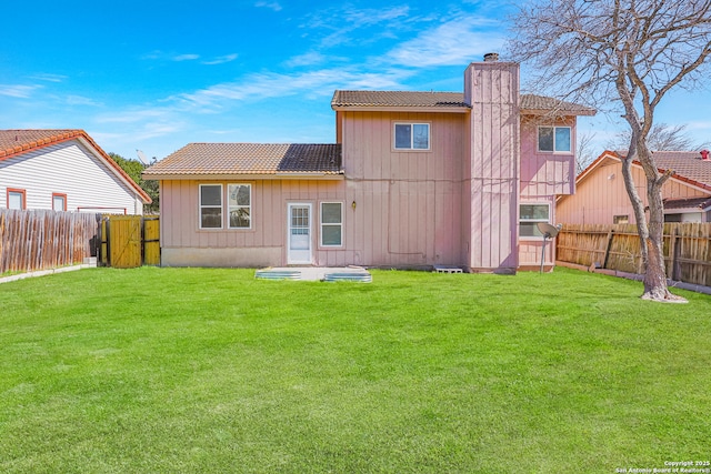 back of house featuring a fenced backyard, a chimney, and a lawn