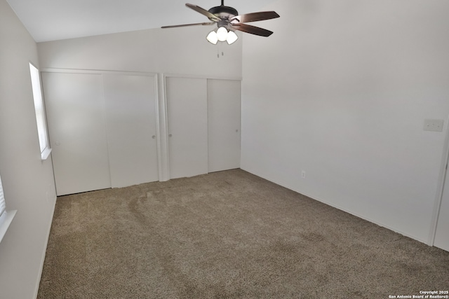 unfurnished bedroom featuring carpet floors, a ceiling fan, vaulted ceiling, and two closets