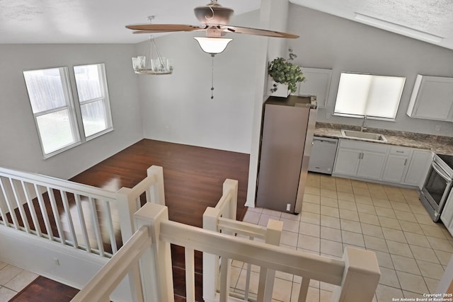 kitchen featuring ceiling fan, light tile patterned floors, a sink, vaulted ceiling, and appliances with stainless steel finishes