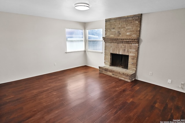 unfurnished living room featuring a brick fireplace, baseboards, and wood finished floors