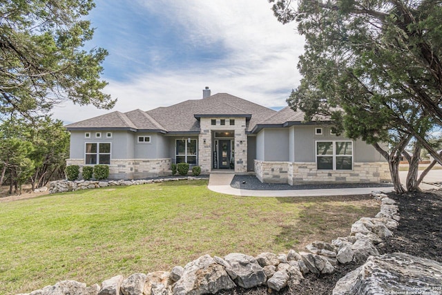 prairie-style house featuring a chimney, stucco siding, a shingled roof, stone siding, and a front lawn