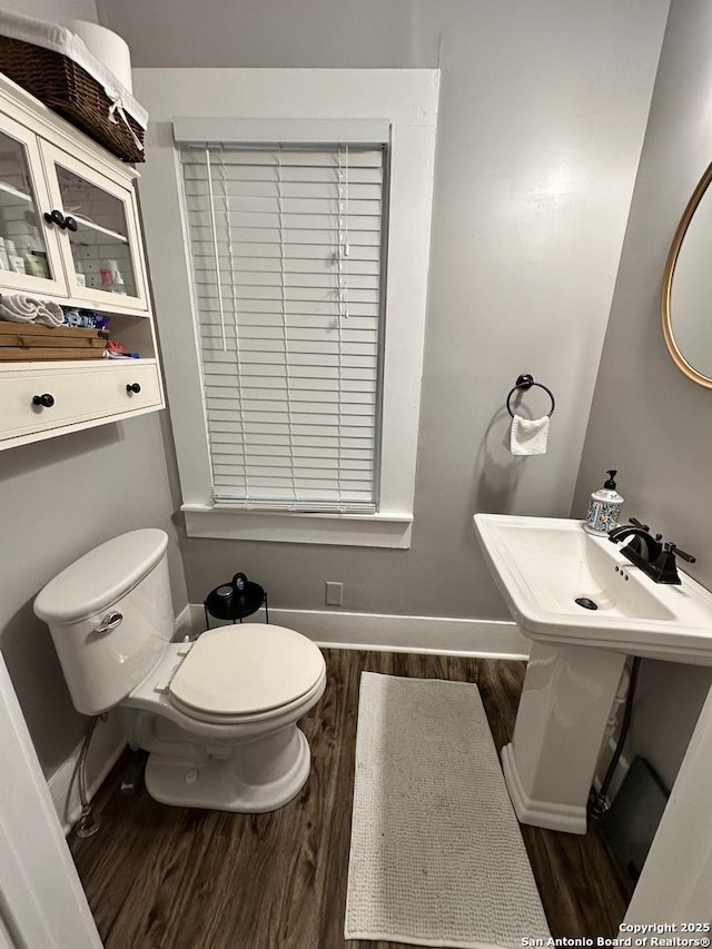 half bath featuring baseboards, toilet, and wood finished floors