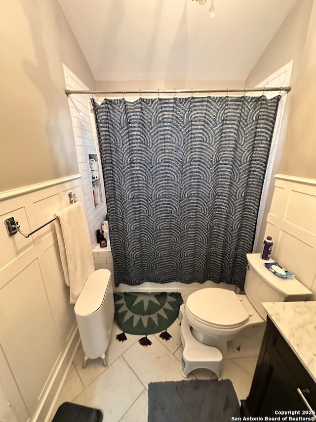 bathroom with lofted ceiling, toilet, a decorative wall, a wainscoted wall, and tile patterned floors