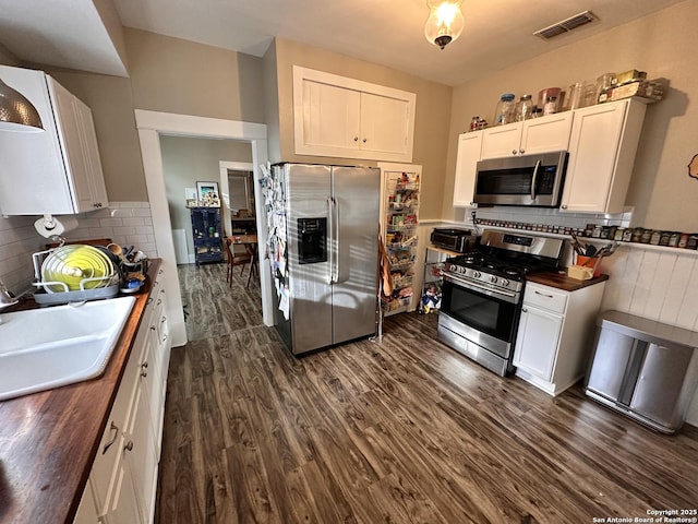 kitchen with dark wood-style floors, stainless steel appliances, visible vents, white cabinets, and a sink