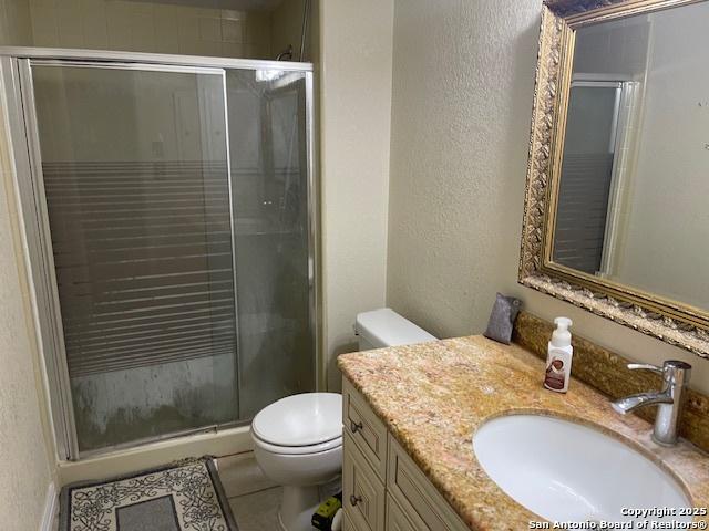 bathroom featuring a textured wall, a stall shower, vanity, and toilet