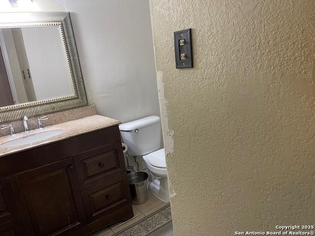 bathroom featuring toilet, a textured wall, tile patterned flooring, and vanity