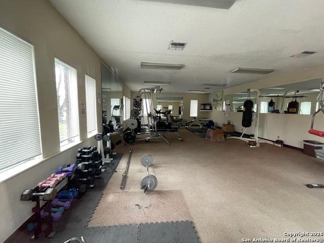 gym with carpet floors, visible vents, and a textured ceiling